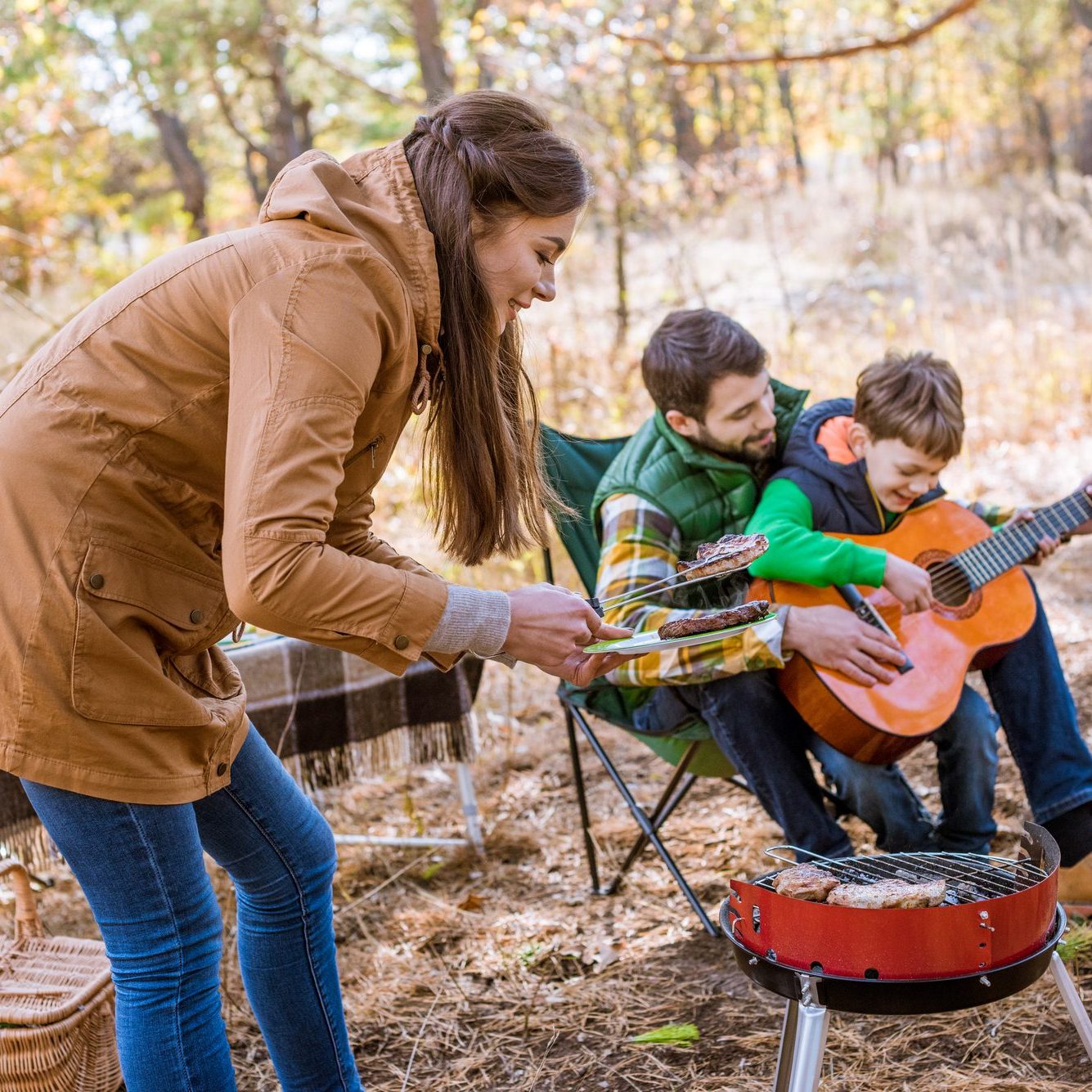Camping in the woods. Mother, Father, and Son with grill and guitar.